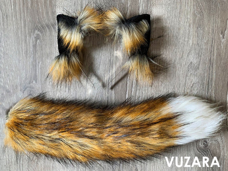 May include: A set of fox tail and ears costume accessories. The tail is brown, black, and white with a fluffy texture. The ears are attached to a headband and are brown, black, and white with a fluffy texture.