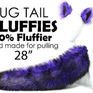 May include: A purple and black faux fur tail, 28 inches long. The tail is attached to a white mannequin with matching purple and black faux fur ear cuffs. The text "Tug Tail Fluffies 60% Fluffier and made for pulling 28"" is visible in the image.