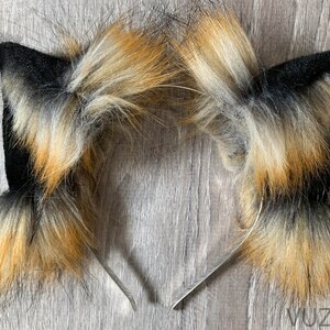 May include: A pair of black and brown furry cat ears headband. The headband is made of metal and the ears are made of faux fur.