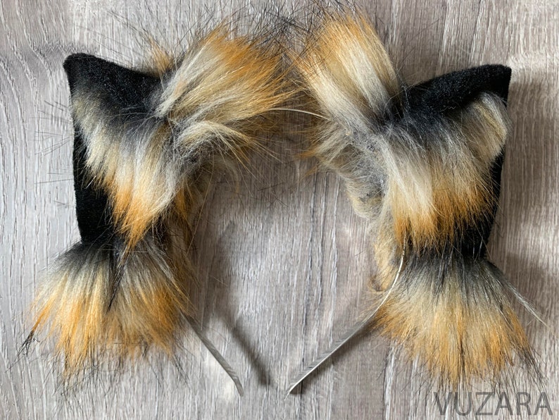 May include: A pair of black and brown furry cat ears headband. The headband is made of metal and the ears are made of faux fur.