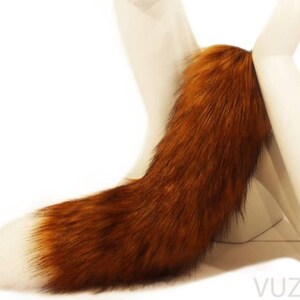 May include: A long, fluffy, brown and white fox tail. The tail is attached to a white stand.