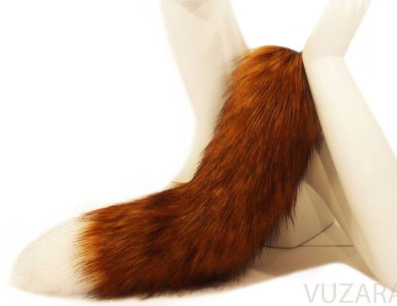 May include: A long, fluffy, brown and white fox tail. The tail is attached to a white stand.