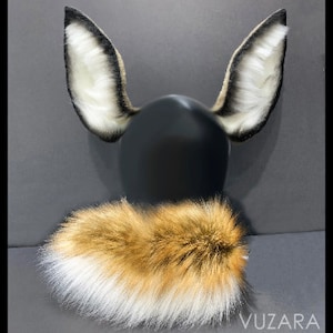 May include: A set of faux fur animal ears and tail. The ears are white with black tips and the tail is a mix of white, brown, and black fur.
