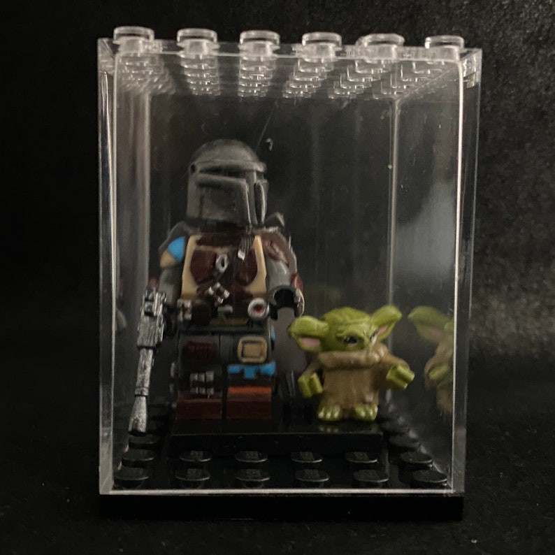 May include: A Mandalorian Lego minifigure with a blaster rifle and a Grogu Lego minifigure in a clear plastic display case.