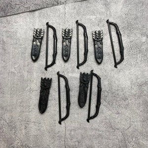 Puede incluir: Seis arcos y flechas de plástico negro de juguete. Cada arco es curvo y tiene una cuerda. Cada flecha tiene una punta de plástico negro y una aljaba con un diseño decorativo.