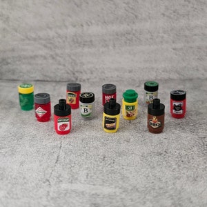 May include: A collection of ten small, colorful, plastic containers with various labels, including "Ketchup", "Mustard", "BBQ", "Hot", and "Pepper".