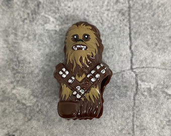Puede incluir: Una figura de Chewbacca marrón y beige con un rostro detallado y textura de pelaje. La figura tiene una bandolera en el pecho y es un artículo de colección de la franquicia Star Wars.