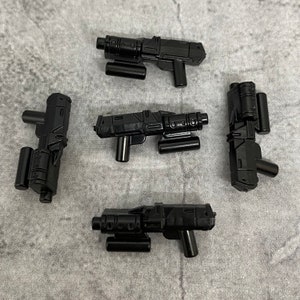 Puede incluir: Cinco pistolas de juguete de plástico negro con detalles intrincados. Las pistolas tienen un diseño futurista y están hechas de un plástico negro mate liso.