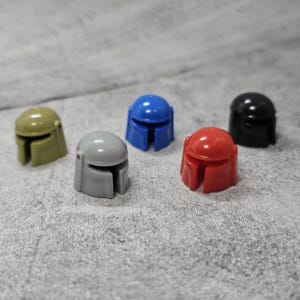 May include: Five plastic helmets in different colors: gray, blue, red, green, and black. The helmets are all the same shape and have a visor.