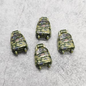 以下が含まれることがあります： 黒いストラップとジッパーが付いた迷彩柄のミニチュアバックパックが4つ。バックパックは硬質プラスチック製で、高さは約5cmです。