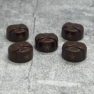 May include: Six brown felt hats with a red star on the front. The hats are arranged in a circle on a grey surface.