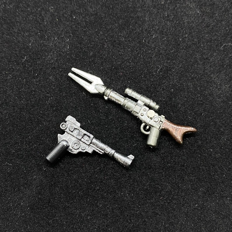 May include: Two silver toy blasters, one with a brown handle and a scope, the other with a black handle and a forked end.