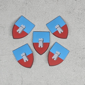 Puede incluir: Cinco fichas en forma de escudo azul y rojo con un diseño de torre blanca. Las torres tienen todas el mismo diseño, pero los escudos están dispuestos en un patrón aleatorio.