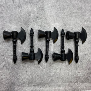 Puede incluir: Cinco hachas de juguete de plástico negro con cabeza de martillo y hoja de hacha. Las hachas están dispuestas en fila sobre una superficie gris texturizada.