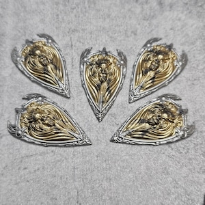 May include: Five silver and gold shield-shaped pendants with a lion's face design. Each pendant has a detailed design with a textured surface.