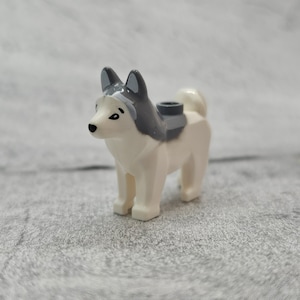 May include: A white and gray plastic toy husky dog with black eyes. The dog has a saddle on its back.