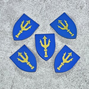 Pode incluir: Cinco escudos azuis com tridentes dourados. Os escudos têm a forma de um escudo heráldico tradicional.