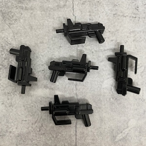 Puede incluir: Cinco pistolas de juguete de plástico negro, algunas con un diseño futurista, otras con un aspecto más tradicional.