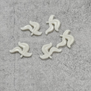 May include: Five white plastic leaves with a stylised design. The leaves are arranged in a circle on a grey textured surface.