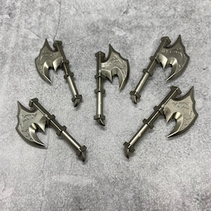 May include: Five silver-colored axe-shaped figurines with intricate designs. The axes have a sharp point and a curved blade. The handles are long and slender.