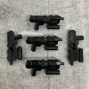 May include: Five black plastic toy guns with a futuristic design. The guns have a barrel, a handle, and a magazine.