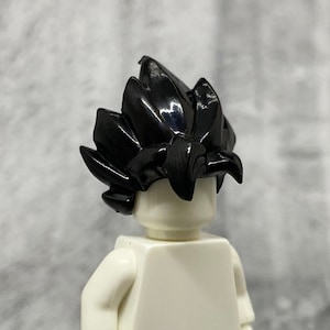 May include: Black Lego minifigure hair piece with a spiky, textured design. The hair piece is made of plastic and has a glossy finish.