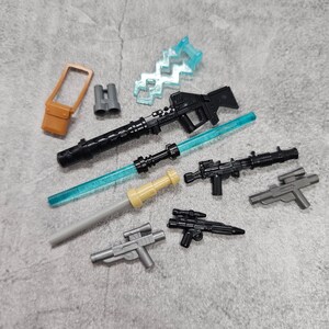 May include: A collection of toy weapons, including a black rifle, a blue lightsaber, a gray lightsaber, a black pistol, a gray pistol, a black and gray pistol, and a brown and black backpack.