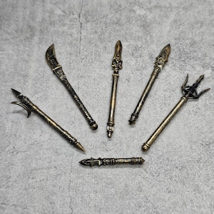 May include: Six decorative, gold-toned, metal weapons with intricate details. The weapons include a sword, a spear, a trident, and three other spears.