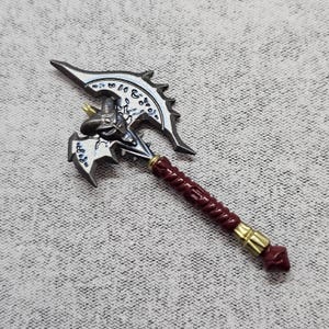 May include: A silver and burgundy fantasy axe with intricate detailing. The axe head features a stylized design with sharp edges and engraved patterns. The handle is a deep burgundy with gold accents, and the overall design suggests a weapon from a fantasy setting.