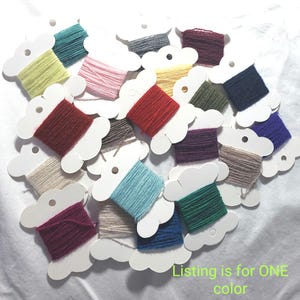 May include: A collection of yarn skeins wrapped around white cardboard bobbins in various colors including red, blue, green, yellow, pink, purple, grey, and beige. The text "Listing is for ONE color" is printed in green at the bottom right.