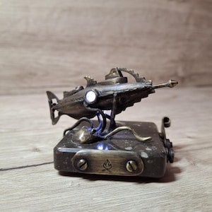 Peut inclure: Une sculpture de sous-marin de style steampunk en bronze avec une lumière blanche brillante. Le sous-marin repose sur une base rectangulaire avec un emblème de flamme. Le design comprend des détails complexes et une esthétique vintage.