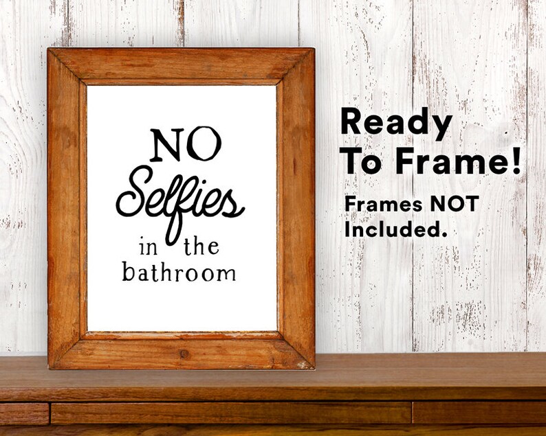 May include: A framed print with the text "NO Selfies in the bathroom" in black lettering on a white background. The frame is brown wood. The text "Ready To Frame! Frames NOT Included." is in black text on a white background.