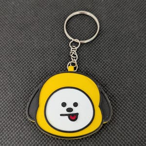 May include: A yellow and black Chimmy keychain with a white face, black eyes, and a red tongue. The keychain has a silver keyring and chain. The Chimmy character is a cartoon dog with a yellow hat and black ears.