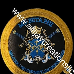 Könnte beinhalten: Gestickter Aufnäher mit goldenem Rand und schwarzem Zentrum. Der Aufnäher zeigt den Text "M. BETA PHI MILITARY FRATERNITY, INCORPORATED" und ein Wappen mit Schwertern, einer Krone und einem Kreuz. Der Aufnäher hat blaue und goldene Akzente.