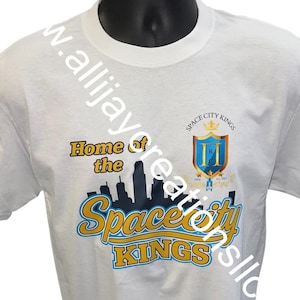 May include: White t-shirt featuring the text "Home of the Space City Kings" in yellow and blue, with a skyline graphic. The shirt also displays a crest with the words "Space City Kings".