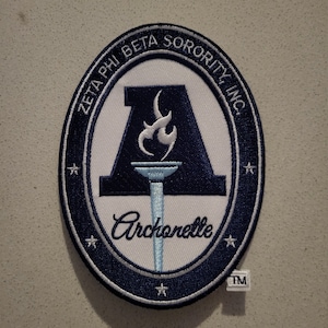 May include: An oval patch with a navy blue border and white interior. The patch features the text "ZETA PHI BETA SORORITY, INC." and "Archonette". A stylized torch and the letter "A" are in the center. The patch has a trademark symbol.