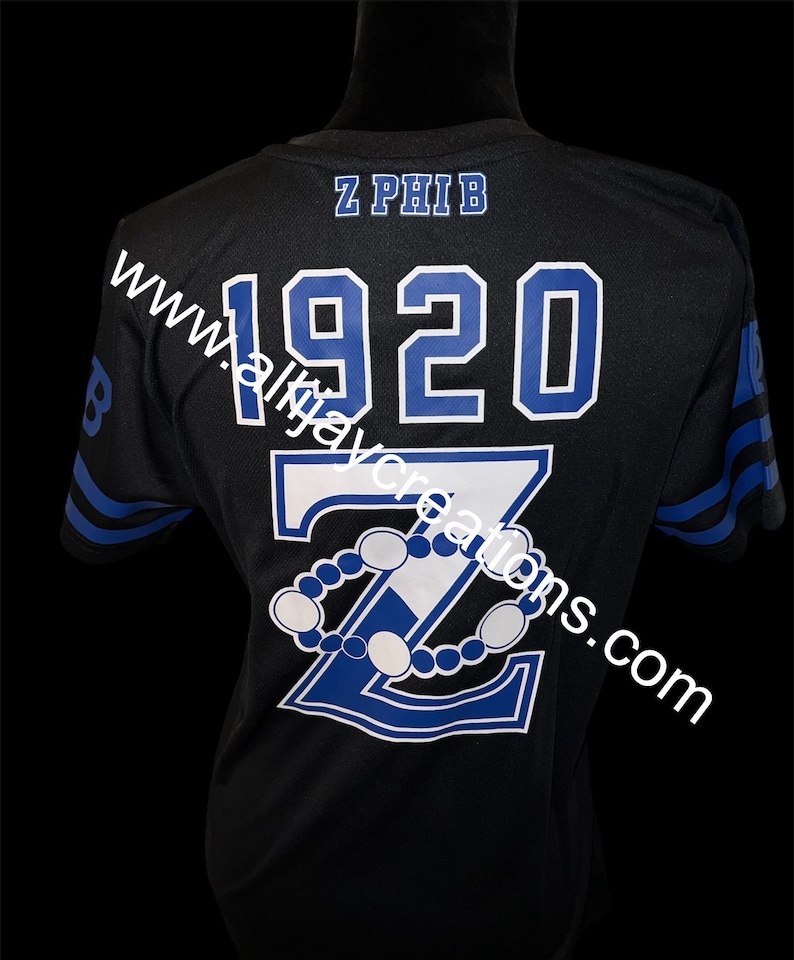 Puede incluir: Camiseta deportiva negra con letras y dise&ntilde;o en azul y blanco. La camiseta presenta el texto "Z PHIB" sobre el a&ntilde;o "1920" y una gran "Z" con un dise&ntilde;o de cuentas. Rayas azules adornan las mangas.