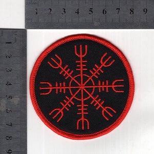 May include: A red and black embroidered patch with a circular design. The design is a compass with eight points, each point is a stylized symbol. The patch is approximately 6.35 cm in diameter.