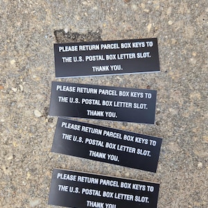 May include: Four rectangular black signs with white text that reads: PLEASE RETURN PARCEL BOX KEYS TO THE U.S. POSTAL BOX LETTER SLOT. THANK YOU. These signs are designed for clear communication regarding the return of postal keys to a designated slot.