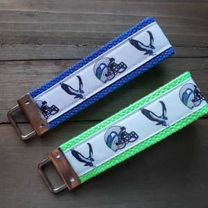 May include: Two keychains with a white background and a blue and green fabric. The keychains feature a football helmet and a bird design.
