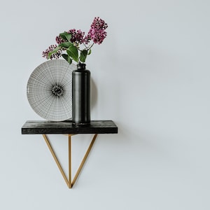 May include: A black and white patterned plate and a black vase with purple flowers on a black shelf with gold metal brackets.