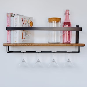 Può includere: Uno scaffale in legno con staffe in metallo nero e un porta bicchieri da vino in metallo nero sotto. Lo scaffale contiene una caraffa di vetro con un coperchio di sughero, una bottiglia di vetro rosa e tre libri di cucina. I libri di cucina sono intitolati "Grandma's Family Traditions", "Vegetarian" e "Veggie Love".