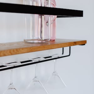 May include: A black metal shelf with a wooden top, holding a glass pitcher with a cork lid and a pink glass bottle.  Four martini glasses hang from the bottom shelf.