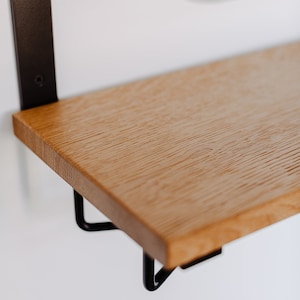 K&ouml;nnte beinhalten: Ein Holzregal mit schwarzen Metallkonsolen. Das Regal ist aus hellem Holz mit nat&uuml;rlicher Maserung.