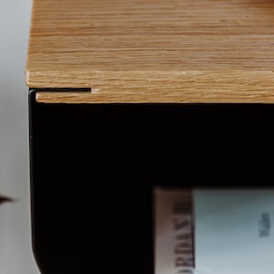 May include: Close-up of a wooden shelf with a black metal frame. The shelf is made of light wood with a natural grain. The metal frame is black and has a simple design.