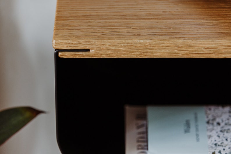 May include: Close-up of a wooden shelf with a black metal frame. The shelf is made of light wood with a natural grain. The metal frame is black and has a simple design.