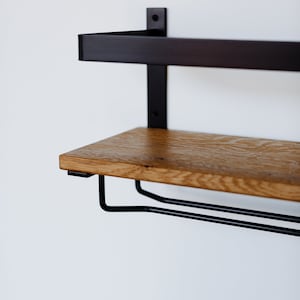 May include: A black metal shelf with a wooden top and a metal wine rack underneath. The shelf is mounted to a white wall.