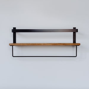 May include: A black metal shelf with a wooden top and a black metal rod underneath. The shelf is mounted to a white wall.