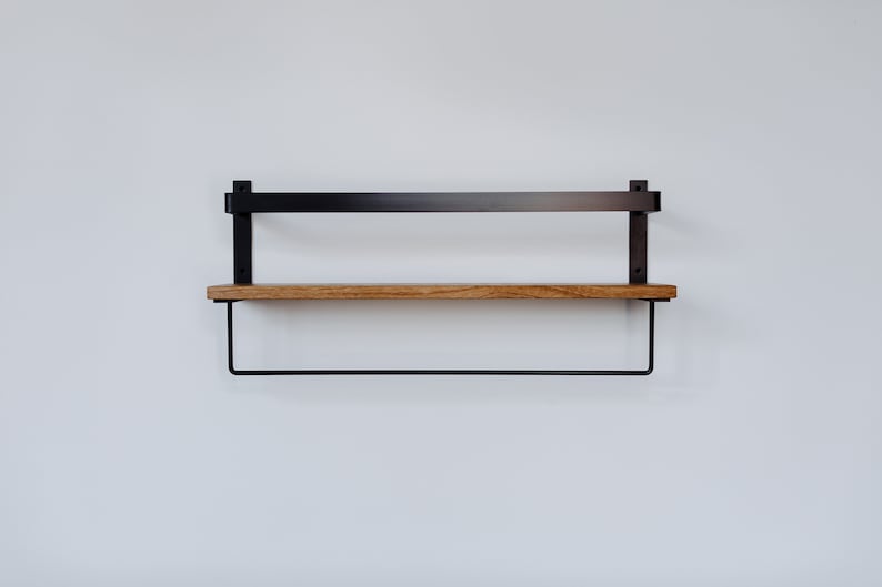 May include: A black metal shelf with a wooden top and a black metal rod underneath. The shelf is mounted to a white wall.