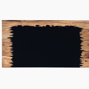May include: A rectangular wooden board with a black, irregular, painted shape in the center.
